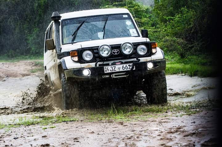 An open safari jeep driving through mud and water on a Kaudulla track in the rain